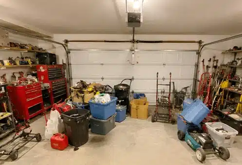Cluttered garage filled with tools, bins, equipment, and household items