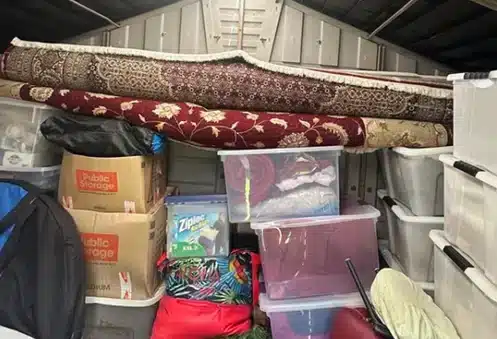Packed storage unit filled with rugs, boxes, bins, and household items