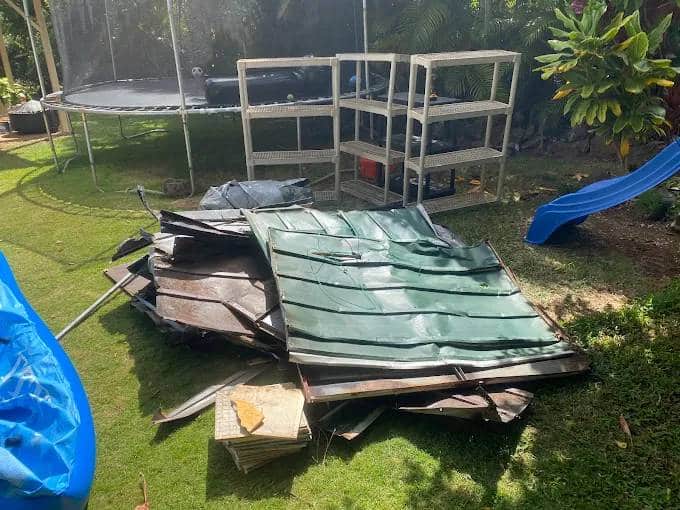 Broken outdoor structure and wooden debris collected in a residential backyard